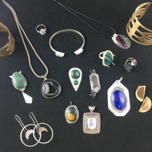 various pieces of jewelry laid out and showing techniques taught at the jewelry school such as bezel setting, pendant making, sawing cuff designs