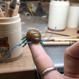 A little wax model of a bug sitting on a finger of the jeweler