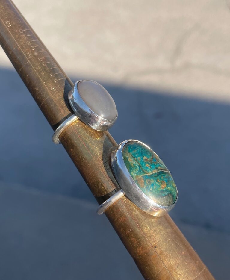 two bezel set rings made in a jewelry making class, featuring cabochon stones. Green and smoky white stones