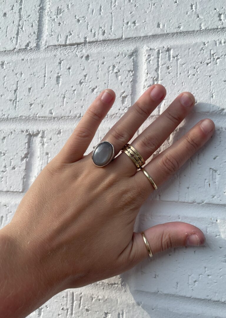Bezel set ring displayed on a hand as a sample for a jewelry making class at The Jeweler's Saw. The ring is a simple design with a grey moonstone set in a bezel