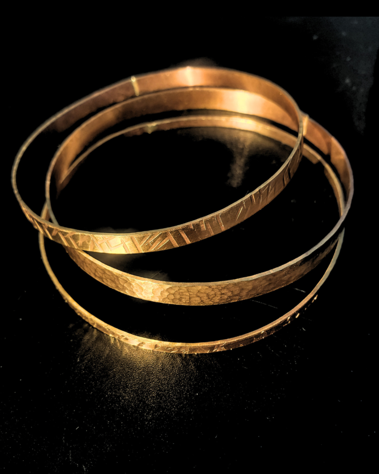 Three brass stacked bangles with hammered textures displayed on a black surface