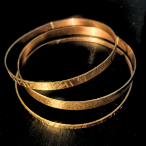 Three brass stacked bangles with hammered textures displayed on a black surface