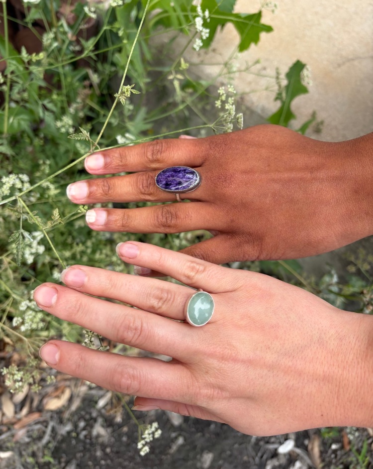 Two handmade bezel-set gemstone rings worn outdoors, featuring oval stones in sterling silver settings made at The Jeweler’s Saw jewelry studio in Austin.